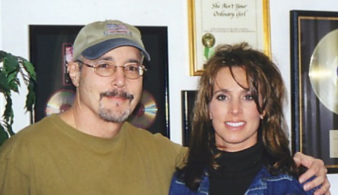 Robert Jason and Tammy in front of his gold records and the framed ‘She Ain’t Your Ordinary Girl’ award